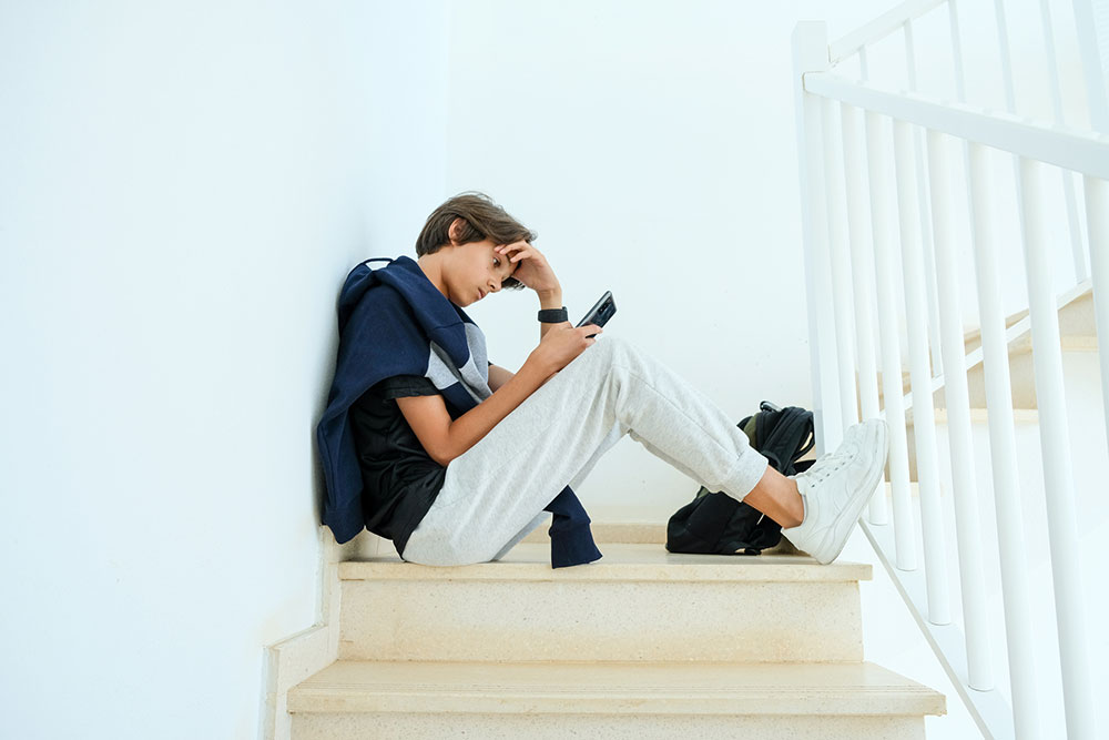 a male teenager sitting at the stairs, looking at his phone