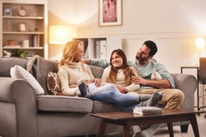 A happy family sitting on the couch communicating and bonding, demonstrating effective listening, hearing, and speaking for harmonious family relationships.